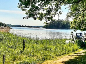 A lakeside view with a boat docked on the right, surrounded by greenery and a clear sky. - 4 Person Holiday Home in Trensum (Trensum)