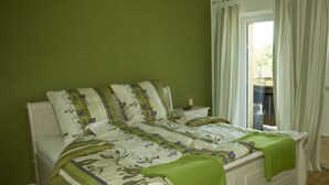 Una cama doble con ropa de cama floral y almohadones verdes en una habitación con paredes verdes y una ventana con cortinas.