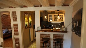 A compact kitchen with a brick wall, wooden ceiling beams, and two bar stools. - Ferieheisel - Everything, Except Usually! (Bad Bergzabern)