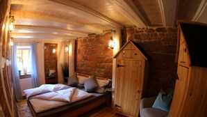 A cozy bedroom with a wooden bed, a stone wall, and a small wooden cabinet. - Ferieheisel - Everything, Except Usually! (Bad Bergzabern)