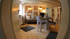 A cozy living room with a sofa, a dining table, and a chair. There is a fireplace with a lamp, and a doormat with "HOME" written on it. - Ferieheisel - Everything, Except Usually! (Bad Bergzabern)