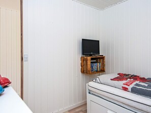 Un dormitorio con una cama, un televisor montado en la pared y una estantería con libros.