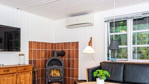 Una habitación acogedora con una estufa de leña, un televisor, una zona de estar con cojines y una ventana con vistas a zonas verdes.