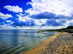 Una playa con un muelle de madera que se adentra en aguas tranquilas, bajo un cielo despejado.