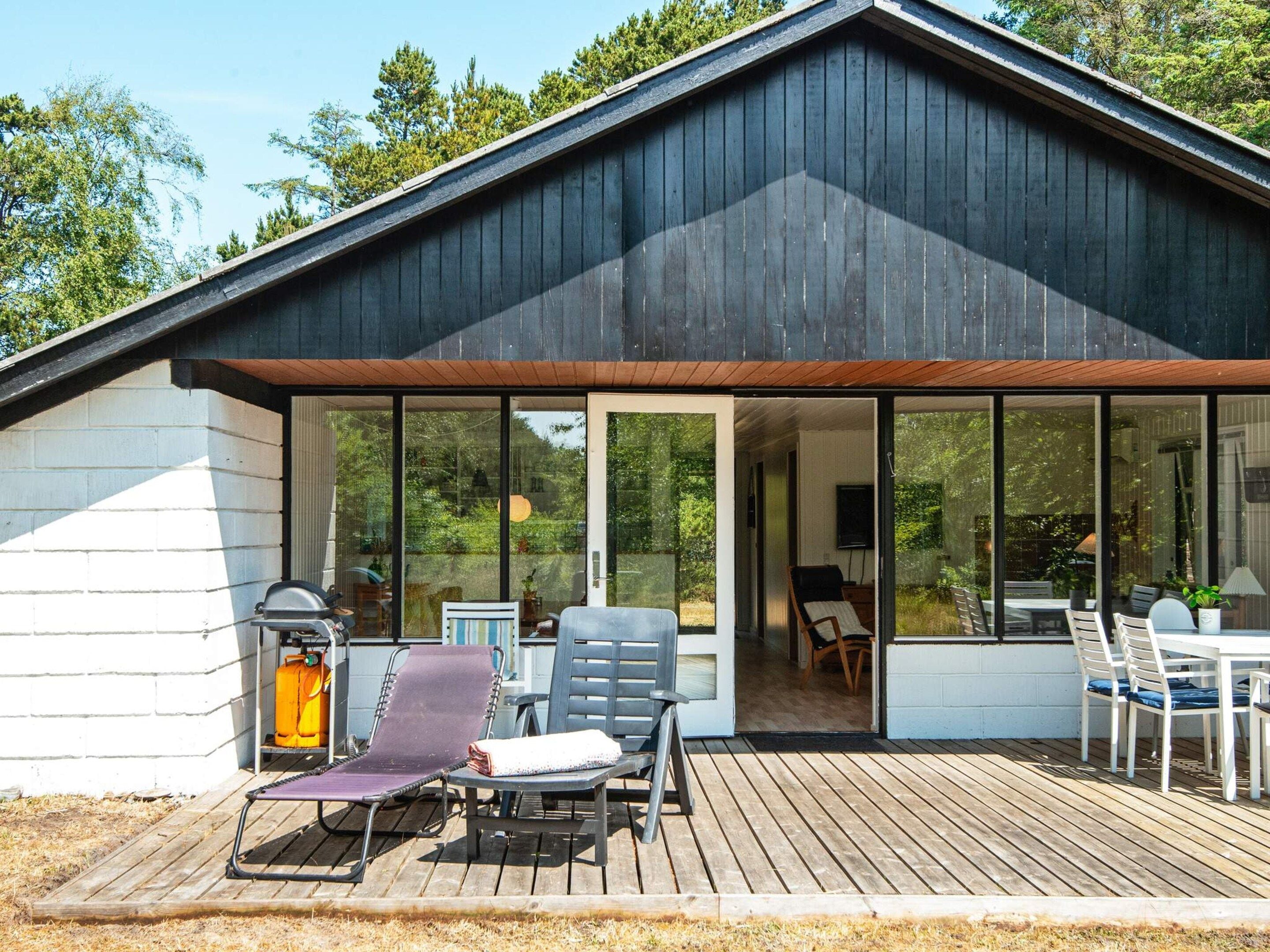 Un bâtiment moderne doté d’une grande entrée en verre, d’une terrasse avec mobilier d’extérieur et d’un barbecue.