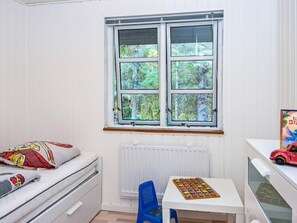 Una habitación infantil con ventana, una cama, un radiador, una mesita con un rompecabezas y un coche de juguete.