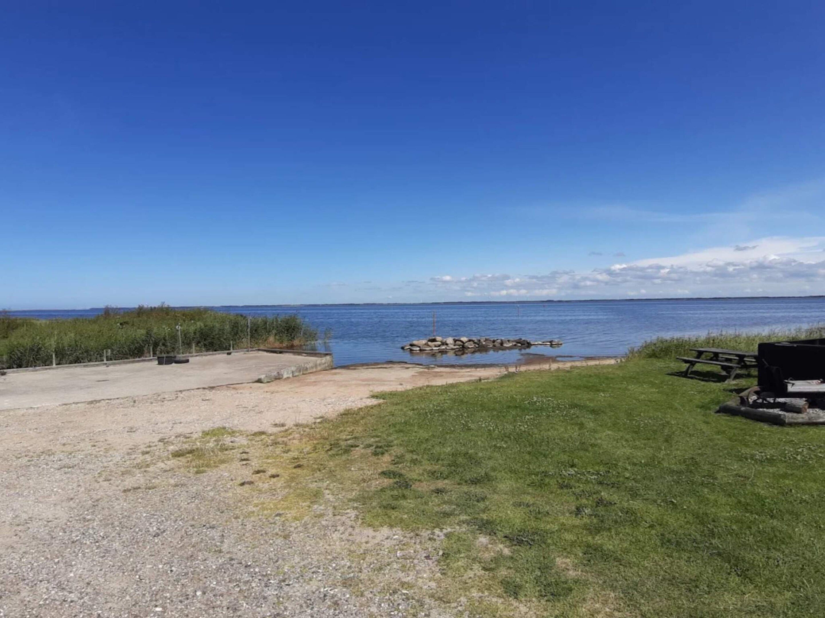 A beachside area with a picnic table, a small dock, and a grassy field.