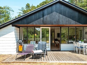 Une maison moderne dotée d’un patio couvert, de grandes fenêtres et de mobilier d’extérieur.