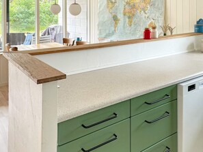 Una cocina con encimera de madera, cajones verdes, un mapa del mundo en la pared y una ventana con vista a zonas verdes.
