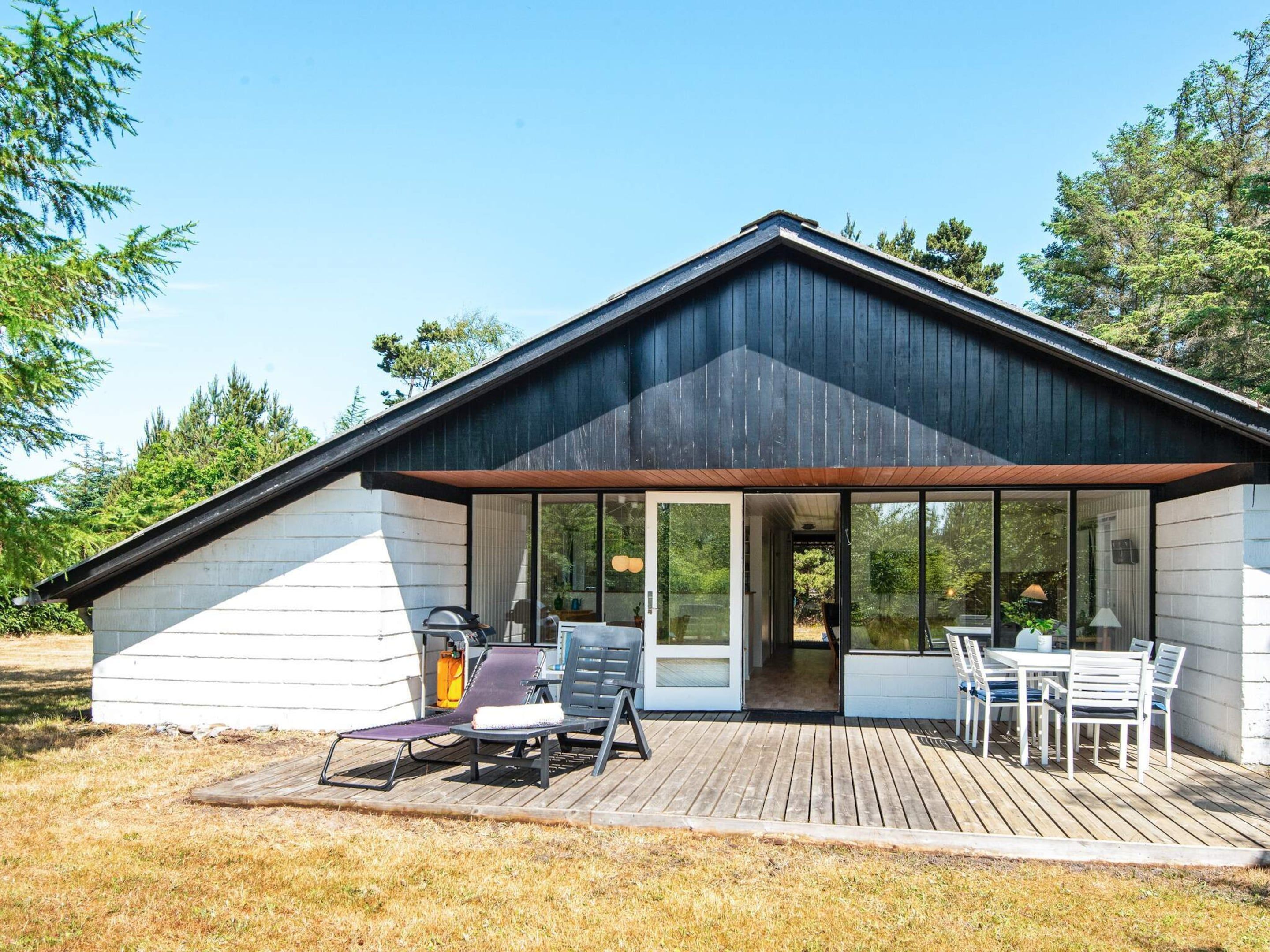 A modern cabin with a deck, outdoor seating, and a large glass door leading to the interior.