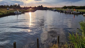 Un río tranquilo con barcos amarrados a la derecha, cielo despejado y un edificio lejano.