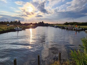 Une rivière paisible, avec des bateaux amarrés sur la rive droite, un ciel dégagé et un bâtiment visible au loin.
