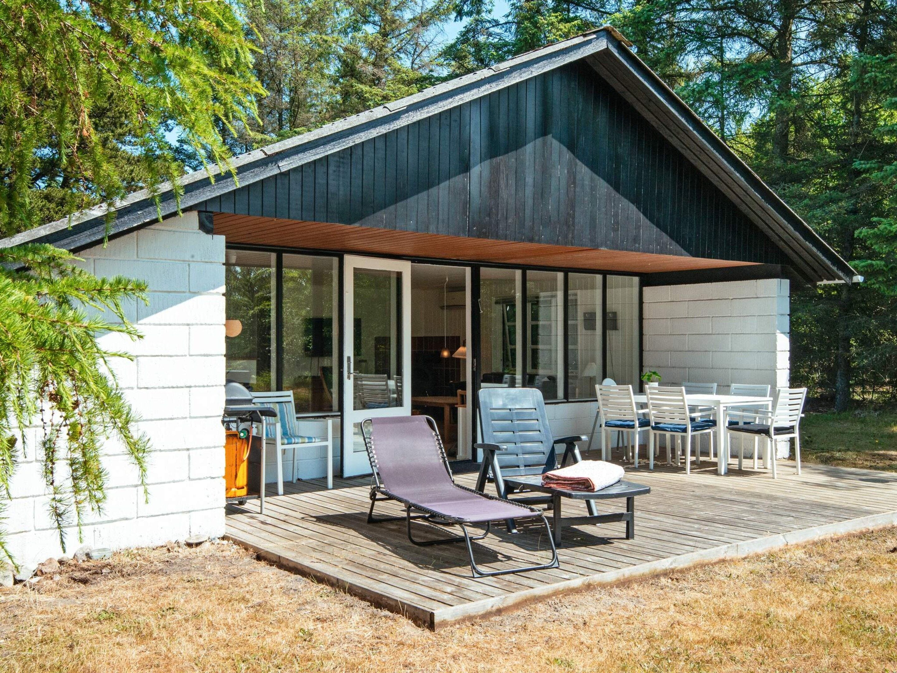 A modern cabin with a deck, outdoor seating, and a glass door entrance.