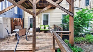 Eine Holzterrasse mit Gartenmöbeln, einem grünen Sofa und einem Hollerker.
