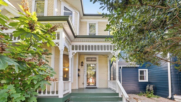 A two-story house with a porch, a front door, and a small window.