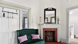 A green velvet sofa with pink cushions, a white door, a fireplace, and a mirror above it.