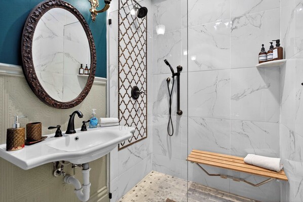 A bathroom with a marble sink, a large mirror, a shower enclosure, and a wooden shelf.