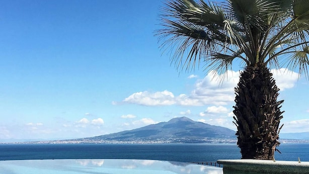 Une piscine à débordement aux eaux cristallines, offrant une vue sur une montagne et, au loin, sur le paysage urbain.
