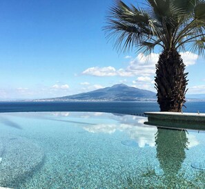 Una piscina infinita cristalina con vistas a una montaña y un paisaje urbano al fondo.
