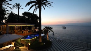 Une propriété située au bord de l’eau, dotée d’une piscine, d’un espace salon extérieur et offrant une vue sur la mer au crépuscule.
