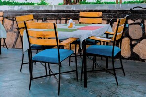 Una mesa con mantel blanco, rodeada de sillas de madera con cojines azules, frente a un fondo de pared de piedra.