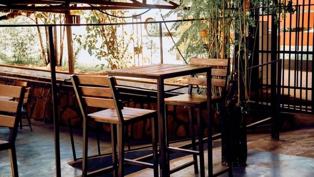 Un café en plein air avec des tables et des chaises en bois, entouré de verdure et délimité par une clôture en métal.