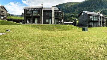 A modern building with a flat roof and large windows, surrounded by a grassy area and hills in the background.