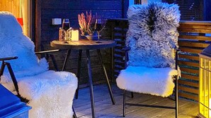 Un rincón exterior acogedor con dos sillones blancos mullidos y una mesita redonda con lámpara y elementos decorativos.