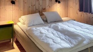 Una cama con ropa de cama blanca en una habitación con paredes de madera y una mesita de noche verde.