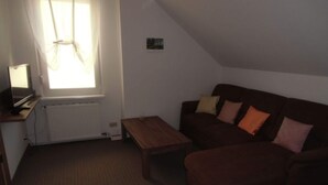 A small living room with a brown sofa, a wooden coffee table, a TV on a stand, and a window with curtains. - Bille Comfortable Holiday Residence (Luckenwalde)