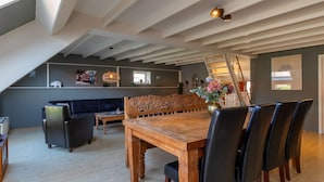 Un espace repas comprenant une table et des chaises en bois, un banc et un luminaire suspendu.