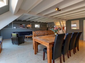 Relax in this spacious loft with a dining table, sofa, and wicker lamp, surrounded by artwork and decorative items.