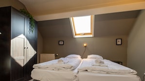 Une chambre avec deux lits, un puits de lumière, un radiateur et une armoire sombre.