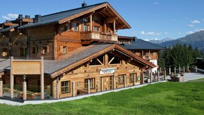 En stuga av trä med en balkong, en skylt med texten ”Hotell” och en bergskedja i bakgrunden.