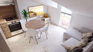 Een moderne keuken met een ingebouwde kookplaat, een eethoek met een ronde tafel en witte stoelen, en een zithoek met een bank en kussens.