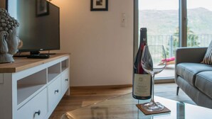 Un soggiorno moderno con una televisione, una bottiglia di vino e un bicchiere su un tavolino in vetro.
