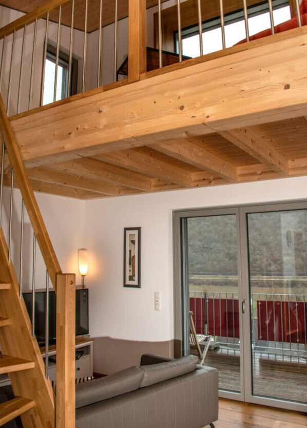A wooden staircase leading to a loft bedroom with a large sliding glass door to a balcony. - Emerald - Holiday Home for (Burgen)