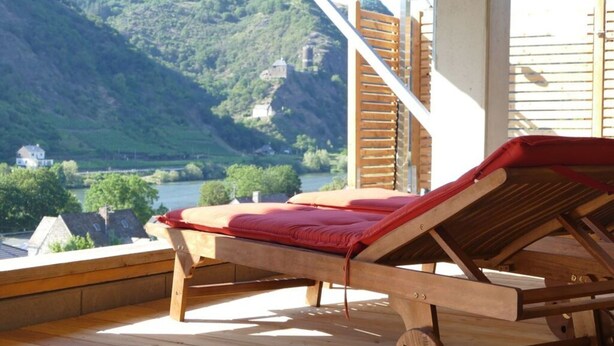 Un pontile in legno con una poltrona da relax rossa che si affaccia su un fiume e delle colline.