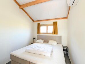 Un dormitorio con cama, mesita de noche, ventana con cortinas y un equipo de aire acondicionado.
