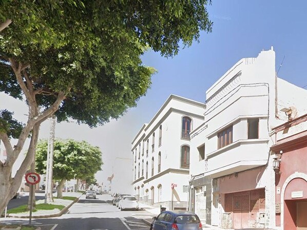 A street view with a building featuring a classical architectural style, a tree-lined sidewalk, and parked cars. - Apartment in Puerto del Rosario Near Playa Chica (Puerto del Rosario)