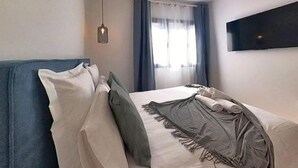 A bedroom with a bed, a hanging light fixture, a window with curtains, and a mounted TV. - Apartment in Puerto del Rosario Near Playa Chica (Puerto del Rosario)
