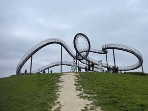 Una escultura metálica en espiral sobre una colina cubierta de césped, con un sendero de tierra que lleva hasta ella.
