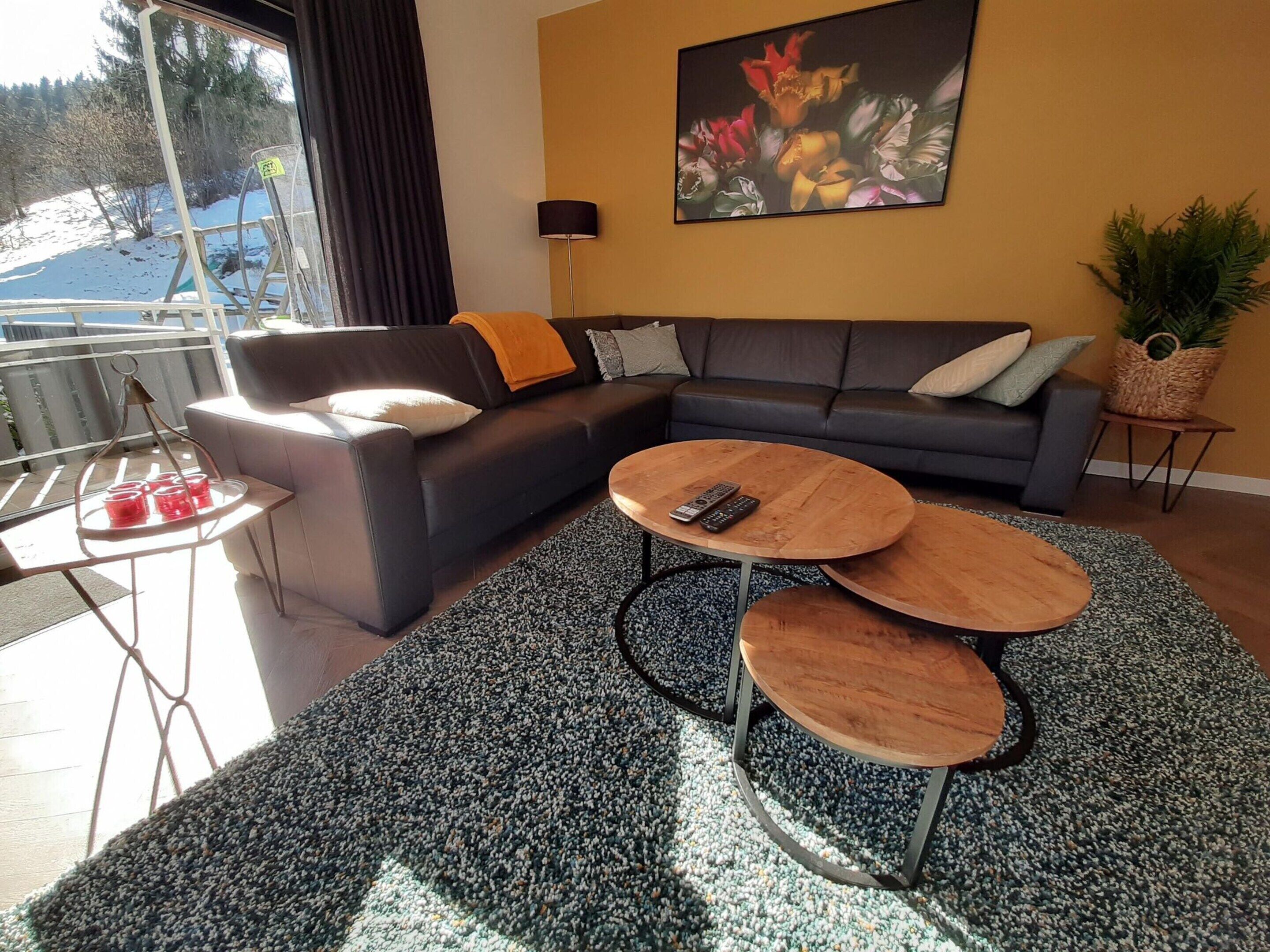 A modern living room with a sectional sofa, two coffee tables, a painting, and a view of the outdoors.