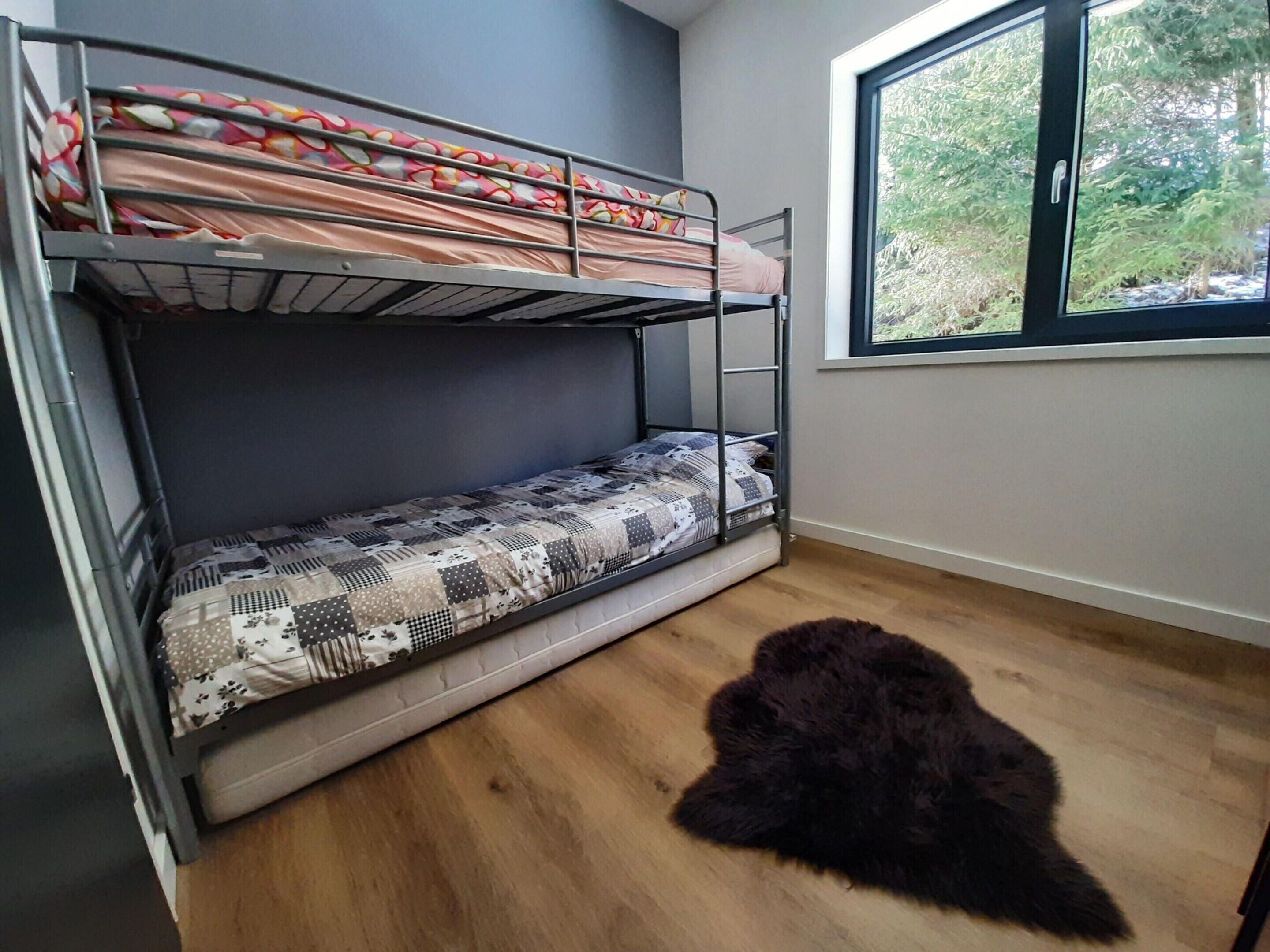 A bunk bed with patterned bedding, a black furry rug on the floor, and a window with a view of trees.