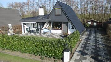A house with a sloped roof, a covered patio with outdoor furniture, and a checkered driveway.