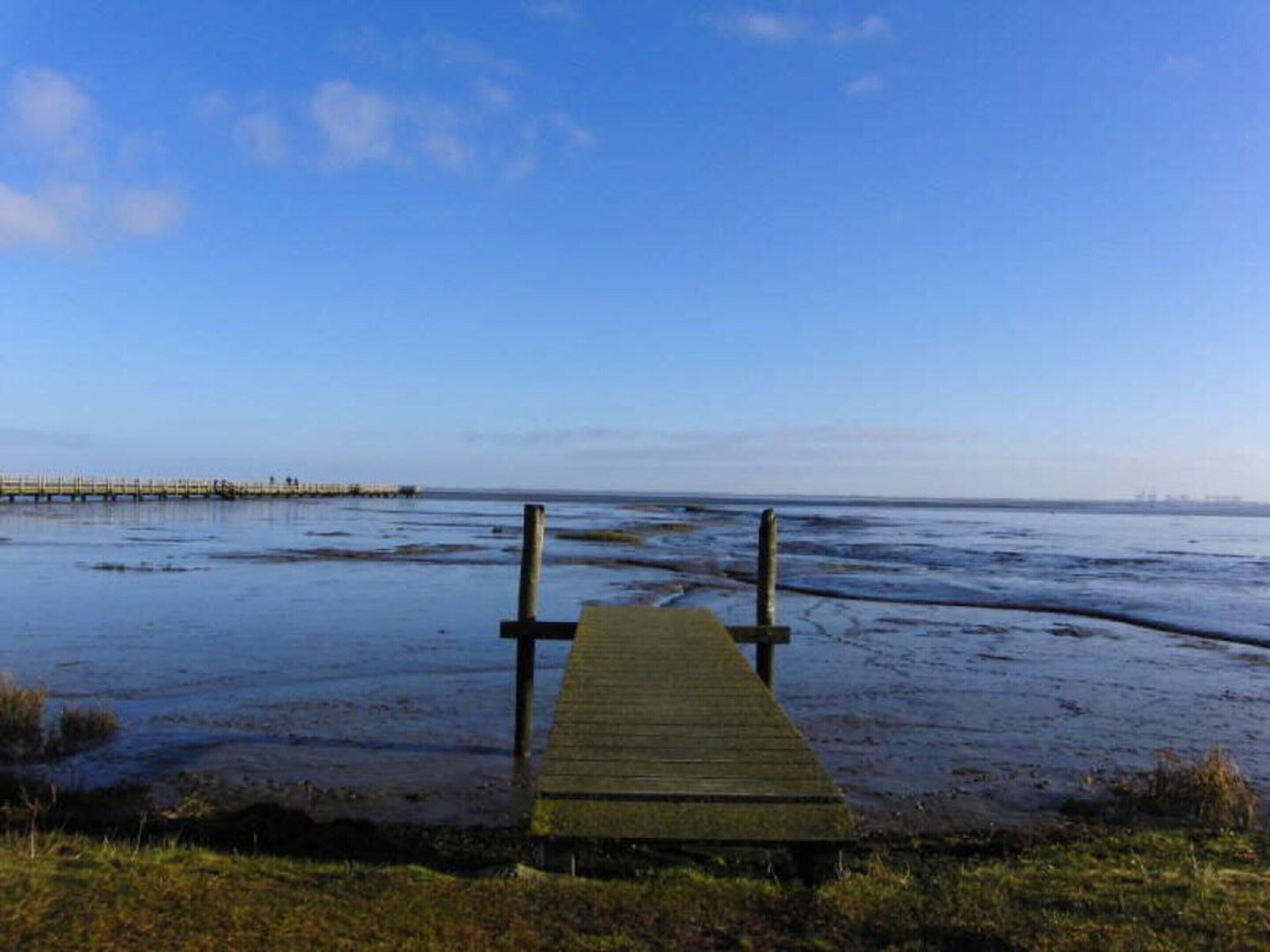 Une jetée en bois s’étendant dans une étendue d’eau, avec un ciel dégagé au-dessus.
