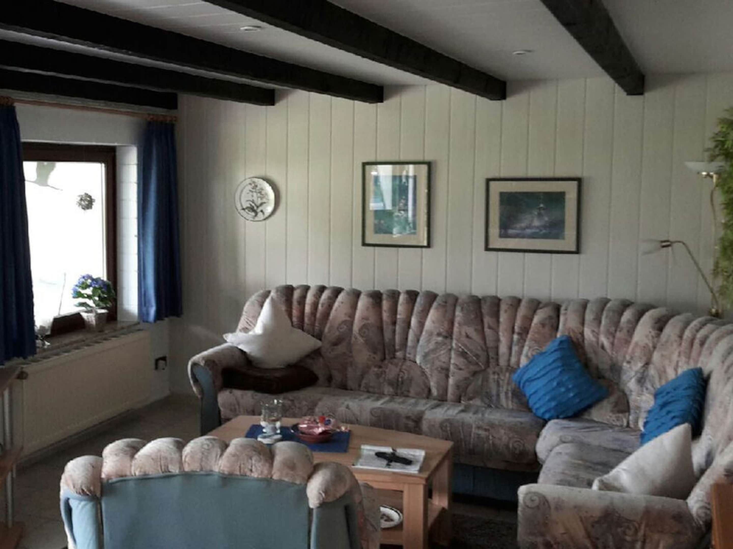 A living room with a sofa, a chair, a coffee table, and a window with curtains.
