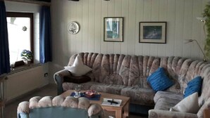 A living room with a sofa, a chair, a coffee table, and a window with curtains. - in the Achtern Diek Holiday Park (Butjadingen)
