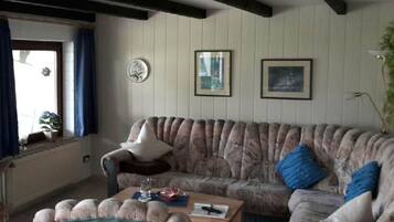 A living room with a sofa, a chair, a coffee table, and a window with curtains.