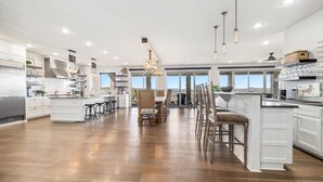 A spacious kitchen with white cabinetry, a central island, and a dining area with bar stools. - Sycamore Ranch - Private MTB Trails - Hot tub! (Eureka Springs)